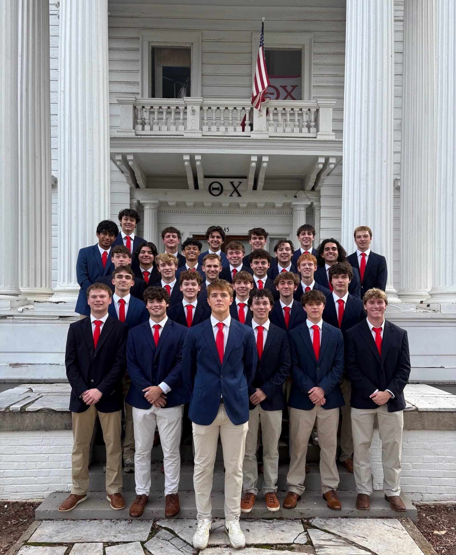 Theta Chi brothers pose in dress clothes in front of their house